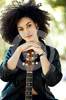 Happy young smiling mixed race female musician enjoying playing her guitar in the park in nature alone. Young hispanic