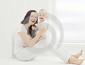 Happy young smiling mother with baby at home in white room