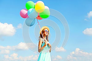 Happy young smiling woman with an air colorful balloons is enjoying a summer sunny day over a blue sky background