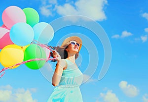 Happy young smiling woman with an air colorful balloons is having fun wearing a summer straw hat over a blue sky background