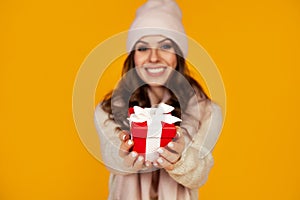 Happy young smiling woman holding and holding red gift box in front, offering and giving Christmas gifts. A girl in a sweater