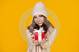 Happy young smiling woman holding and holding red gift box in front, offering and giving Christmas gifts. A girl in a sweater