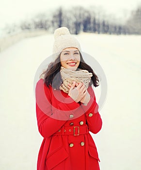 Happy young smiling woman wearing a red coat, knitted hat and scarf in winter