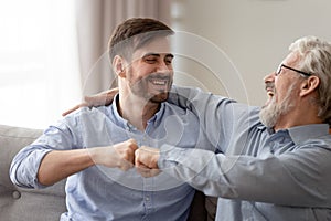 Happy young son and old father fists bumping, having fun