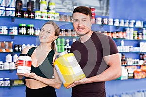 Happy young sporty people standing in store, holding big can of sport nutrition