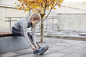 Happy young sporty woman tying shoelaces outdoors