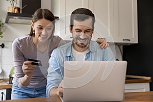 Happy young spouses paying online by card via e-banking app