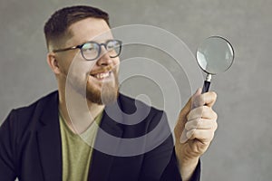 Happy young student or businessman in glasses looking through a magnifying glass