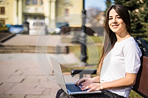 Happy young student with laptop sitting on the bench