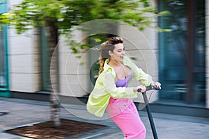 Happy Young Stylish Woman Riding Scooter And Smiling. Photo is Blurred To Emphasize Speed