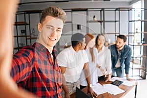 Happy young successful team of multi-ethnic businesspeople making selfie photo in coworking space and smiling looking at