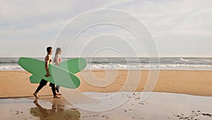 Happy young surfers couple with surfboards walking along the beach