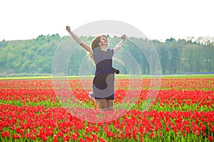 Happy young teen girl jumping up against a spring tulip field.