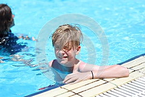 Happy young teenage boy relaxing on the side of swimming pool during summer vacation