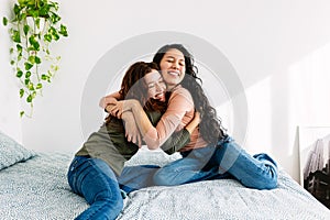 Happy young teenage girls hugging each other sitting on bed