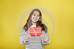 Happy young teenager girl holds red gift certificate on yellow background. People lifestyle holidays concept