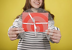 Happy young teenager girl holds red gift certificate on yellow background. People lifestyle holidays concept