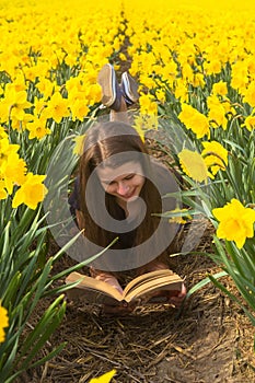Happy young teenager girl reads book among flowers.