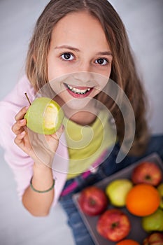 Happy young teenager girl sitting on the floor eating an apple