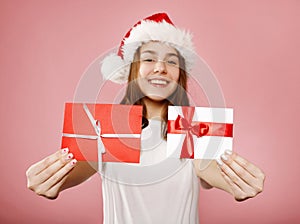 Happy young teenager girl in white t-shirt and santa claus red hat hold two different gift certificates isolated on pink