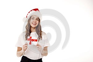 Happy young teenager girl in white t-shirt and santa claus red hat holds gift certificate isolated on white background. People