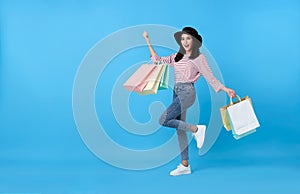 Happy young thai asian female carrying with both arms raised in a ecstatic gesture and shopping bags on blue copy space background