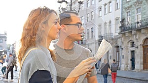 Happy young tourists couple holding a paper map of ancient European city early in the morning on empty square and