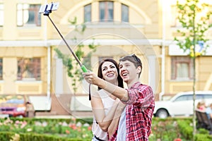Happy young tourists couple taking a selfie with smartphone on the monopod in city.