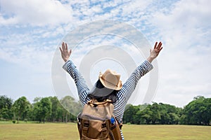 Happy young traveler woman backpacker arms up and enjoying a beautiful of nature at grass field greenery fresh air,Freedom