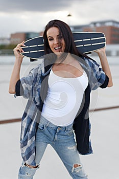 Happy young urban woman posing with longboard behind head