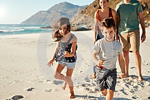 Happy young white family on holiday exploring a beach together, front view, full length, crop