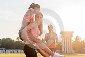 Happy young wiman piggybacking her friend at stadium.