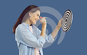 Happy young woman aims dart arrow at target to show concept of setting goals and strategy