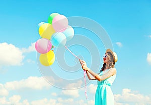 Happy young woman with an air colorful balloons is having fun wearing a summer straw hat over a blue sky background