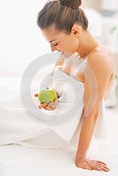 Happy young woman with apple sitting on massage table