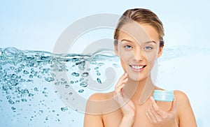 Happy young woman applying cream to her face