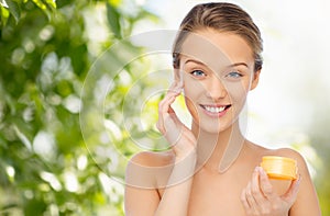 Happy young woman applying cream to her face