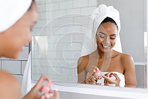 Happy young woman applying face cream in bathroom