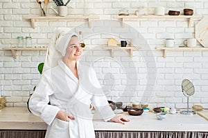 Happy young woman applying face scrub on her face in her home kitchen