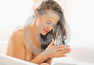 Happy young woman applying hair conditioner in bathtub