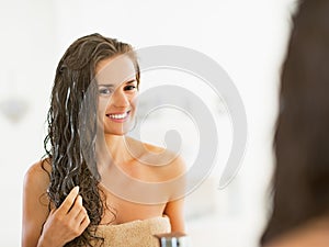 Happy young woman applying hair mask in bathroom