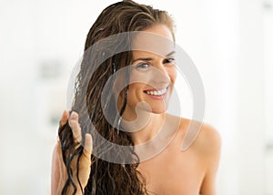 Happy young woman applying hair mask in bathroom