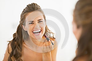 Happy young woman applying lipstick in bathroom