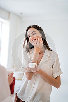Happy young woman applying rejuvenation face cream with collagen under eye