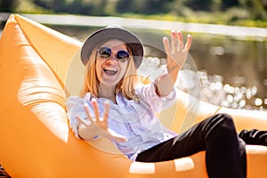 Happy young woman with arms raised celebrating something while relax on inflatable mattress near mountain lake. Portrait