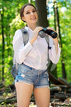 Happy young woman as a backpacker in forest with binoculars