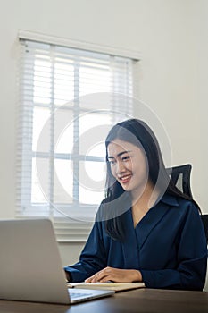 Happy young woman asian working from home distance on laptop taking notes. Smiling business woman lady using computer