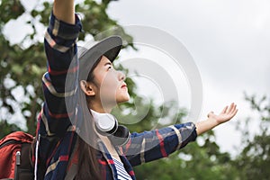 Happy young woman with backpack and hat, Traveler standing with raised arms and enjoying a beautiful nature