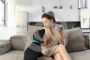 Happy young woman in bathrobe, enjoys spending time with her dog at home, eating cereals, having breakfast with puppy