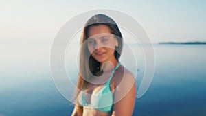 Happy young woman at beach. Girl tourist is wearing bikini on vacation gesturing peace sign at camera